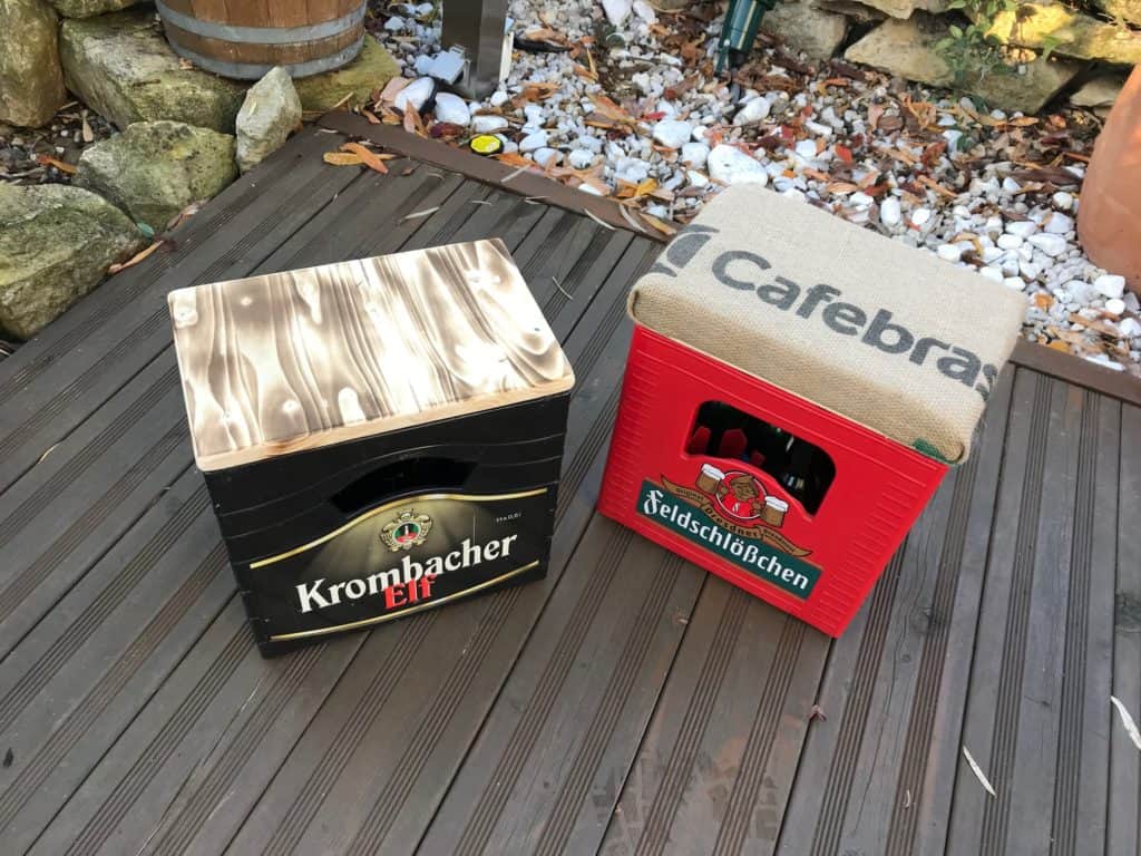 gebrannte Holzbierkastensitz und gepolsteter Kaffeebierkastensitz auf Terrassenboden mit Holzverkleidung und Kieselbett im Hintergrund.